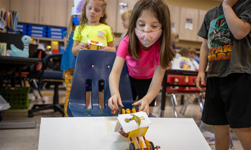 A girl releases a toy car down a ramp